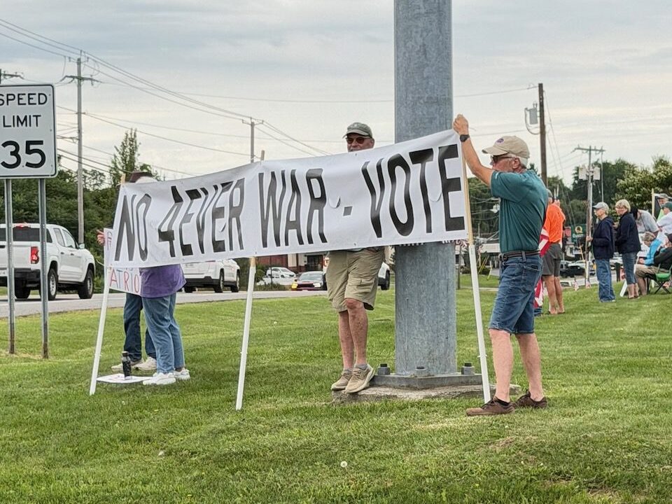 Protesters holding 'No Forever War - Vote' banner on roadside