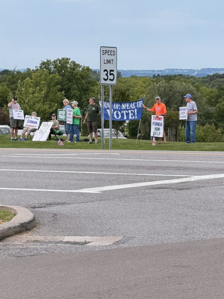 Protesters holding political signs near a roadside speed limit sign