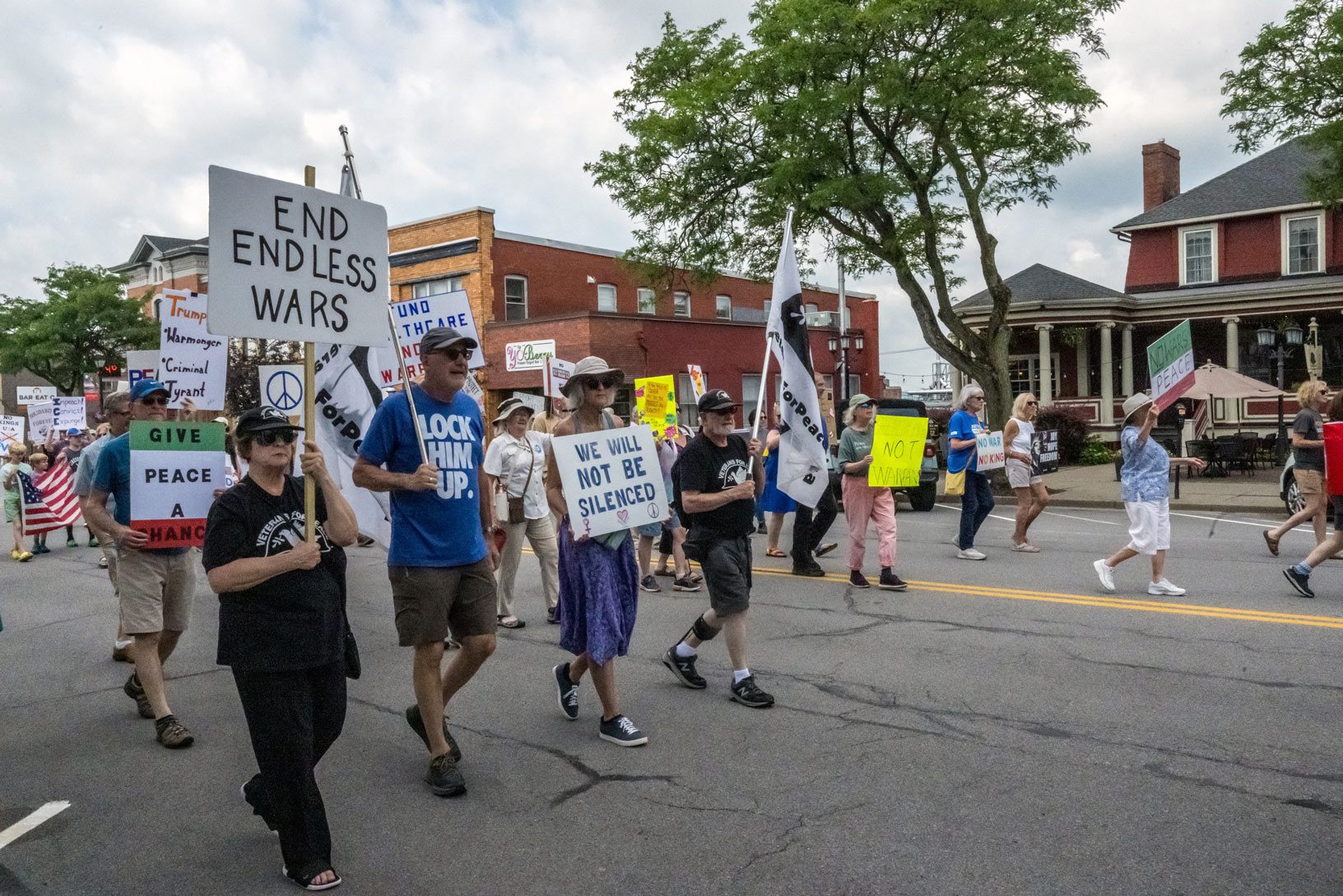 Diverse group of protesters marching down a Geneseo street holding anti-war signs.