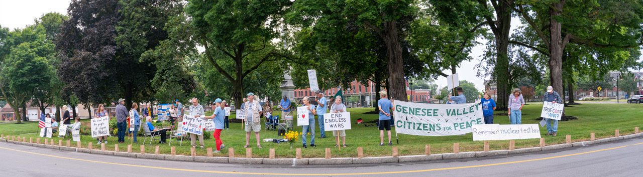 Panoramic view of GVCP members in a line holding peace signs and banners at the Hiroshima vigil.