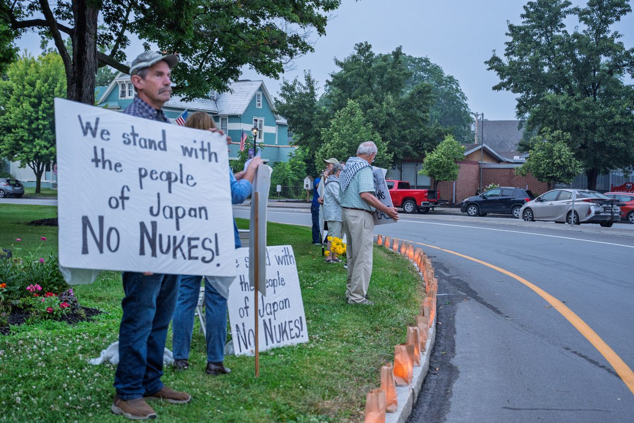 Group holding No Nukes signs next to paper lanterns lining the curb at the Avon vigil.